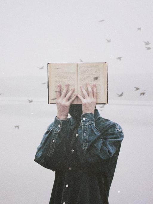 Ein Mann hält sich ein Buch vor sein Gesicht, im Hintergrund fliegt ein Schwarm kleiner Vögel durch das Bild.