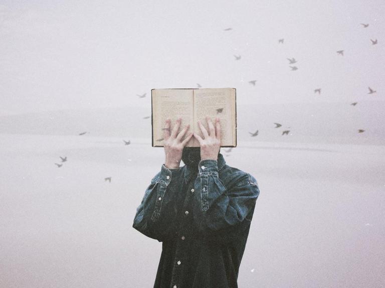 Ein Mann hält sich ein Buch vor sein Gesicht, im Hintergrund fliegt ein Schwarm kleiner Vögel durch das Bild.