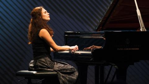Eine Frau mit langen roten Haaren sitzt am Flügel und spielt mit geschlossenen Augen.