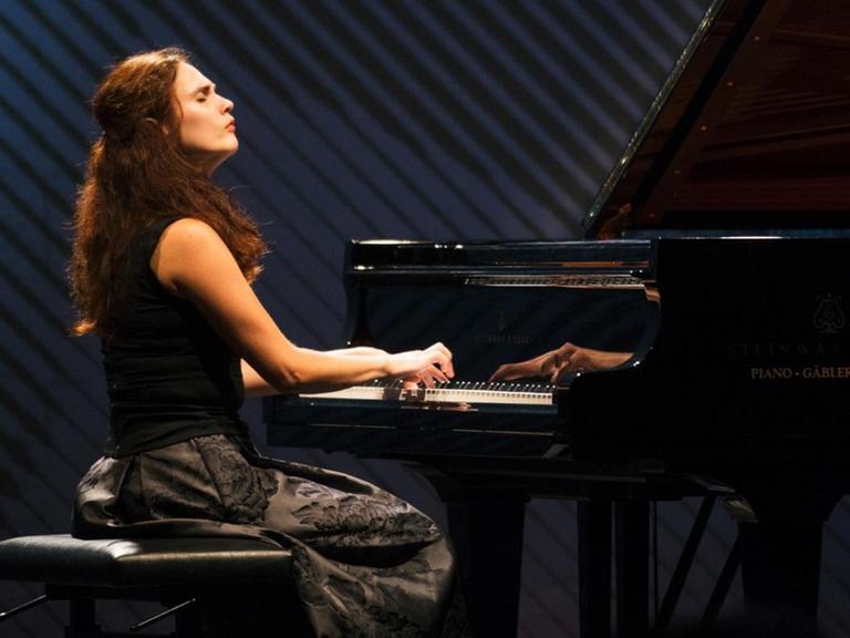 Eine Frau mit langen roten Haaren sitzt am Flügel und spielt mit geschlossenen Augen.