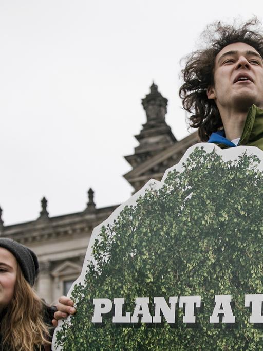 Ein junger Mann steht vor dem Bundestag und hält ein Plakat hoch, auf dem steht: "Plant a tree"