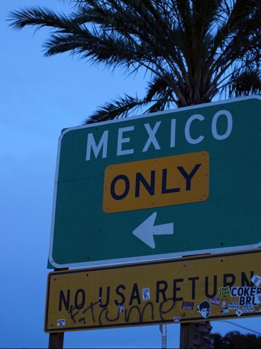 Auf einem Wegweiser vor einer Palme stehen die Worte "Mexiko Only - No USA Return".