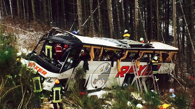 Der beschädigte Bus ist gegen eine Reihe Bäume an einem Abhang geprallt, Rettungskräfte sichern ihn. Der beschädigte Bus ist gegen eine Reihe Bäume an einem Abhang geprallt, Rettungskräfte sichern ihn.