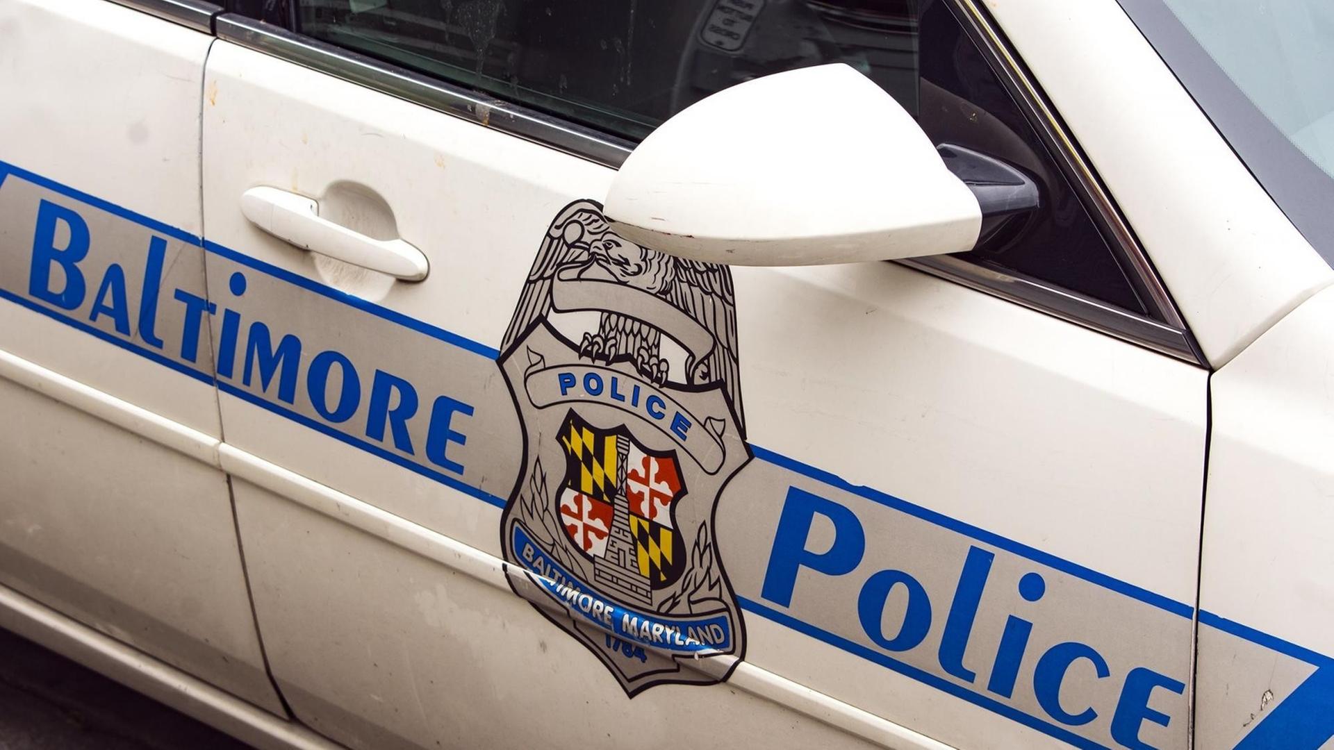Das Bild zeigt die Tür eines weißen Polizei-Fahrzeugs. Auf dem Aufdruck steht "Baltimore Police", in der Mitte sieht man das Polizeiwappen.