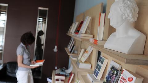 Eine Frau steht vor einem Bücherregal und hält ein Buch in der Hand.