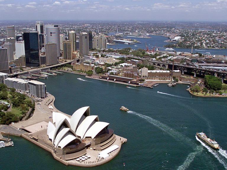 Blick aus der Luft auf das Opernhaus (vorn), den Hafen und die Skyline der Innenstadt von Sydney. Das weltberühmte Opernhaus von Sydney wird von der UNESCO als Welterbe-Stätte anerkannt. Das beschloss das Welterbe-Komitee am Donnerstag (28.06.2007) auf seiner Sitzung im neuseeländischen Christchurch. Das Gremium hob zur Begründung den anhaltenden Einfluss des aus drei muschelähnlichen Dächern bestehenden Bauwerks auf die Architektur hervor.