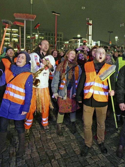 Anti-Pegida-Demonstranten in Dresden mit Warnwesten und Besen. Dresdner Künstler fegten am 5. Januar 2015 mit einem Kehraus - einem Neujahrsputz - den Platz der Pegida-Kundgebung symbolisch sauber.