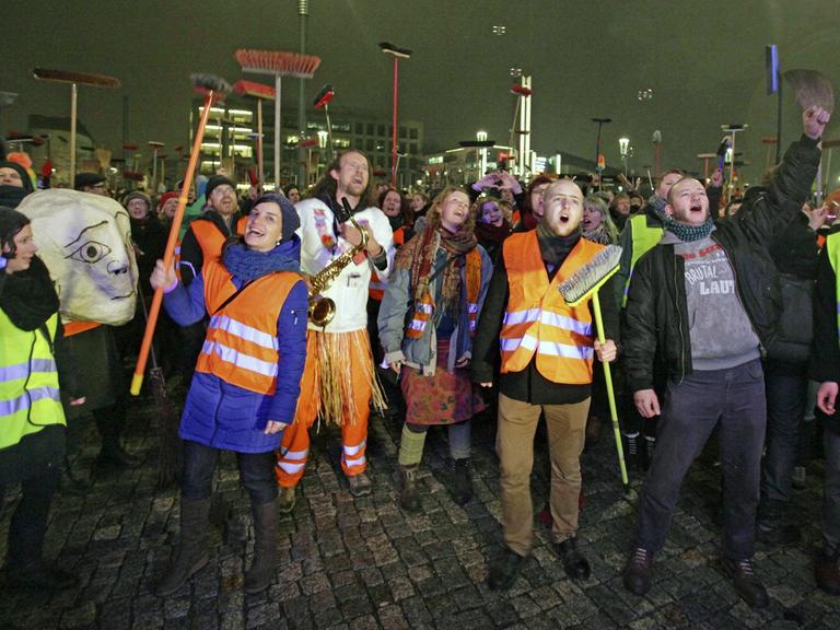 Anti-Pegida-Demonstranten in Dresden mit Warnwesten und Besen. Dresdner Künstler fegten am 5. Januar 2015 mit einem Kehraus - einem Neujahrsputz - den Platz der Pegida-Kundgebung symbolisch sauber.