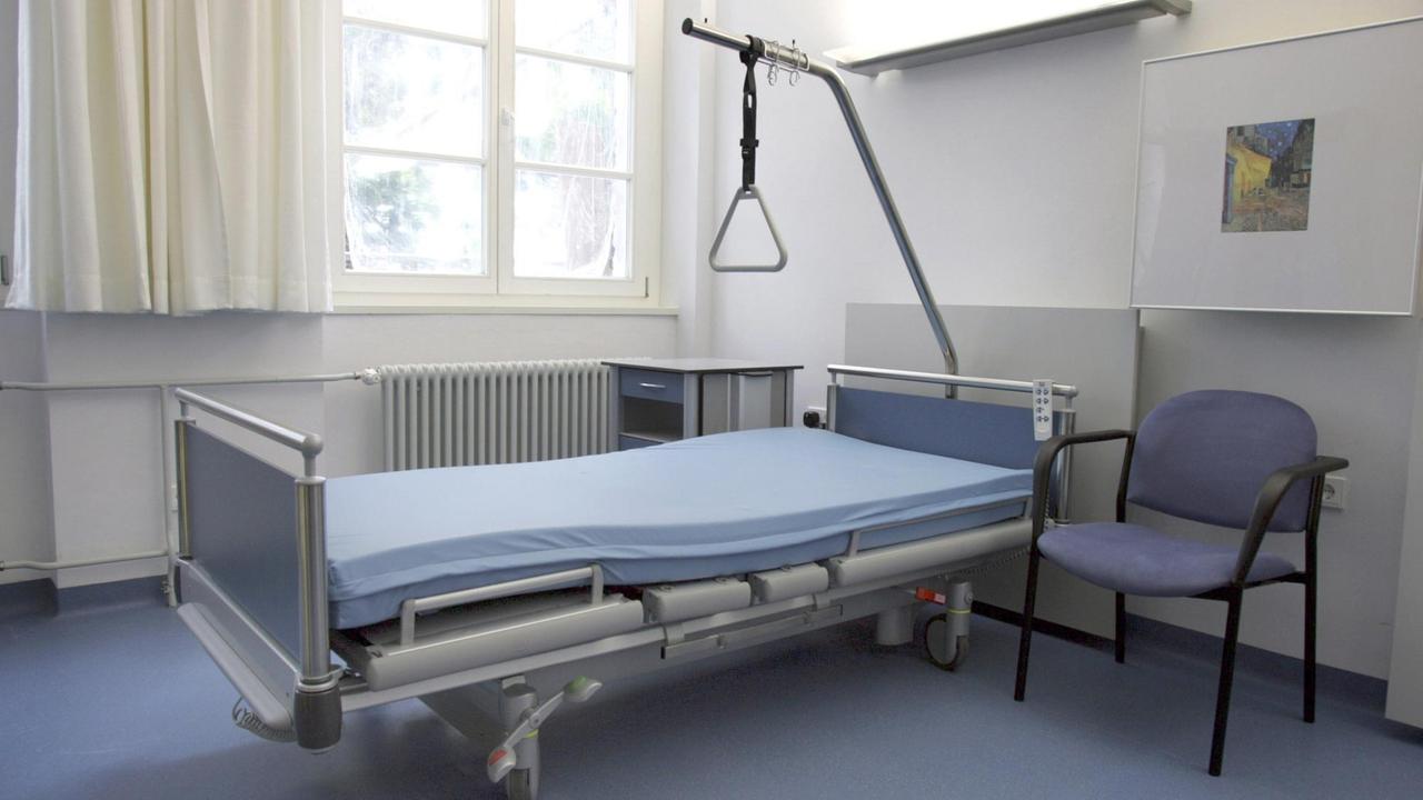 Leeres Krankhausbetten in einem großen Krankenzimmer mit blauem Fußboden.