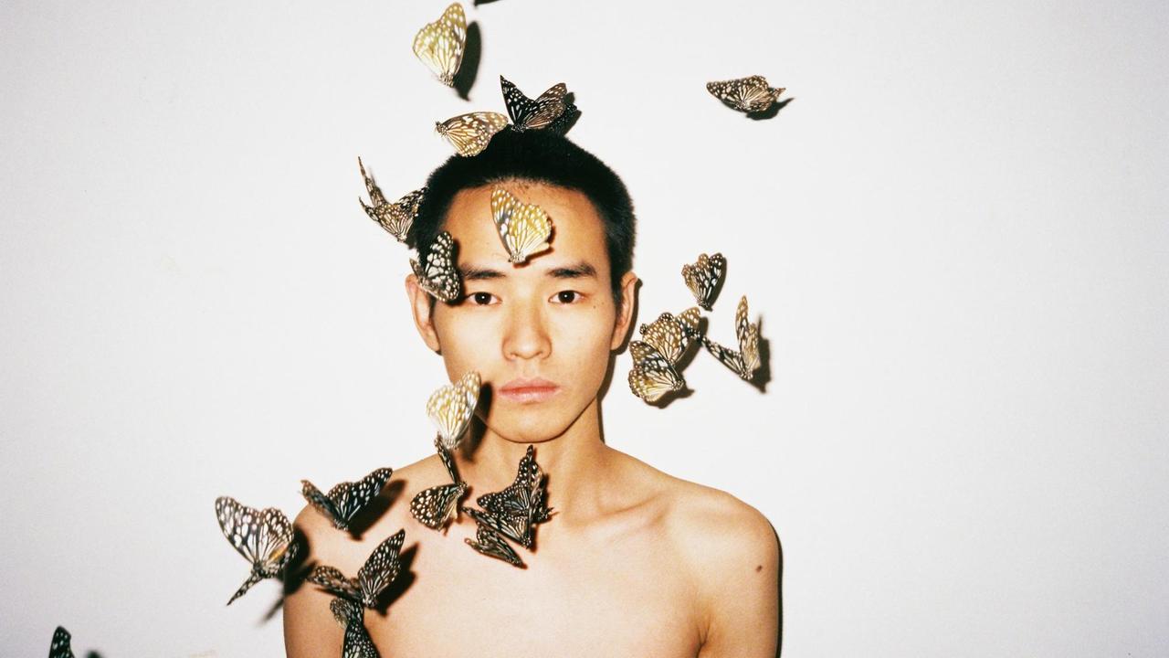 Ein Mann umgeben von einem Schwarm Schmetterlingen, fotografiert von Ren Hang.