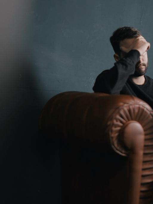 Ein Mann sitzt traurig auf einem Sofa und hält die Hand vor sein Gesicht
