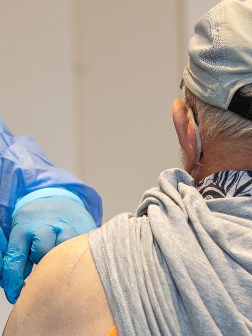 Eine Krankenschwester von einem mobilen Impfteam impft einen älteren Mann in einer Sporthalle im sächsischen Pirna.