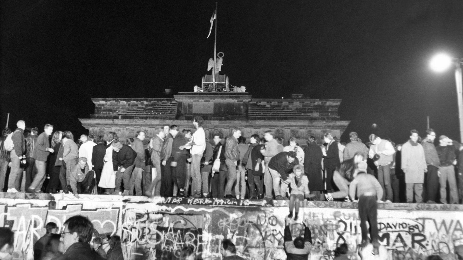 9. November 1989, Menschen stehen auf der Berliner Mauer vor dem Brandenburger Tor und feiern den Mauerfall