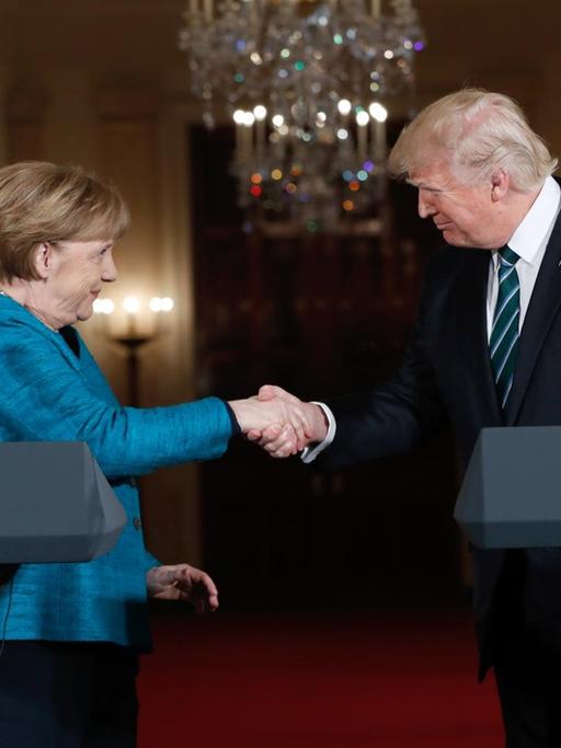 Merkel und Trump stehen hinter ihren Rednerpulten und geben sich lächelnd die Hand.