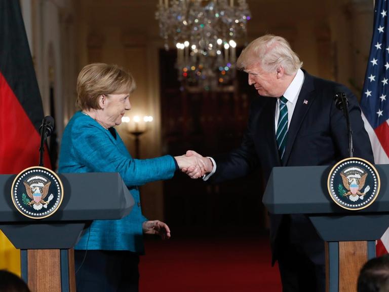 Merkel und Trump stehen hinter ihren Rednerpulten und geben sich lächelnd die Hand.