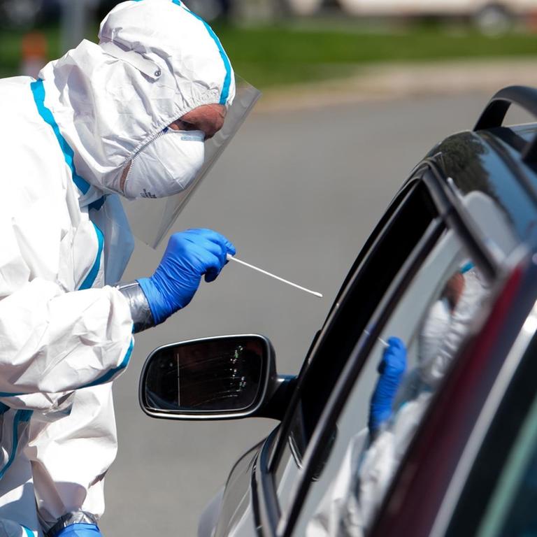 Bayern, Bergen: Ein Mann im Schutzanzug nimmt an einem Corona-Testzentrum an der Autobahn 8 (A8) an der Rastanlage Hochfelln-Nord einen Abstrich bei einem Autofahrer. Bayern, Bergen: Ein Mann im Schutzanzug nimmt an einem Corona-Testzentrum an der Autobahn 8 (A8) an der Rastanlage Hochfelln-Nord einen Abstrich bei einem Autofahrer.