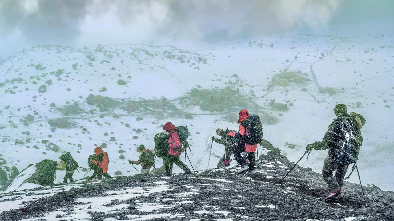Mehrere Bergsteiger in voller Ausrüstung klettern über einen verschneiten Pass.