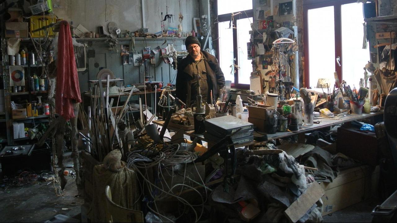Michael Vogel in seiner Puppen-Werkstatt. Überall sind Teile von Handpuppen, Werkzeug und Material verteilt. Es gibt kaum einen freien Ort. Alles ist vollgestellt.