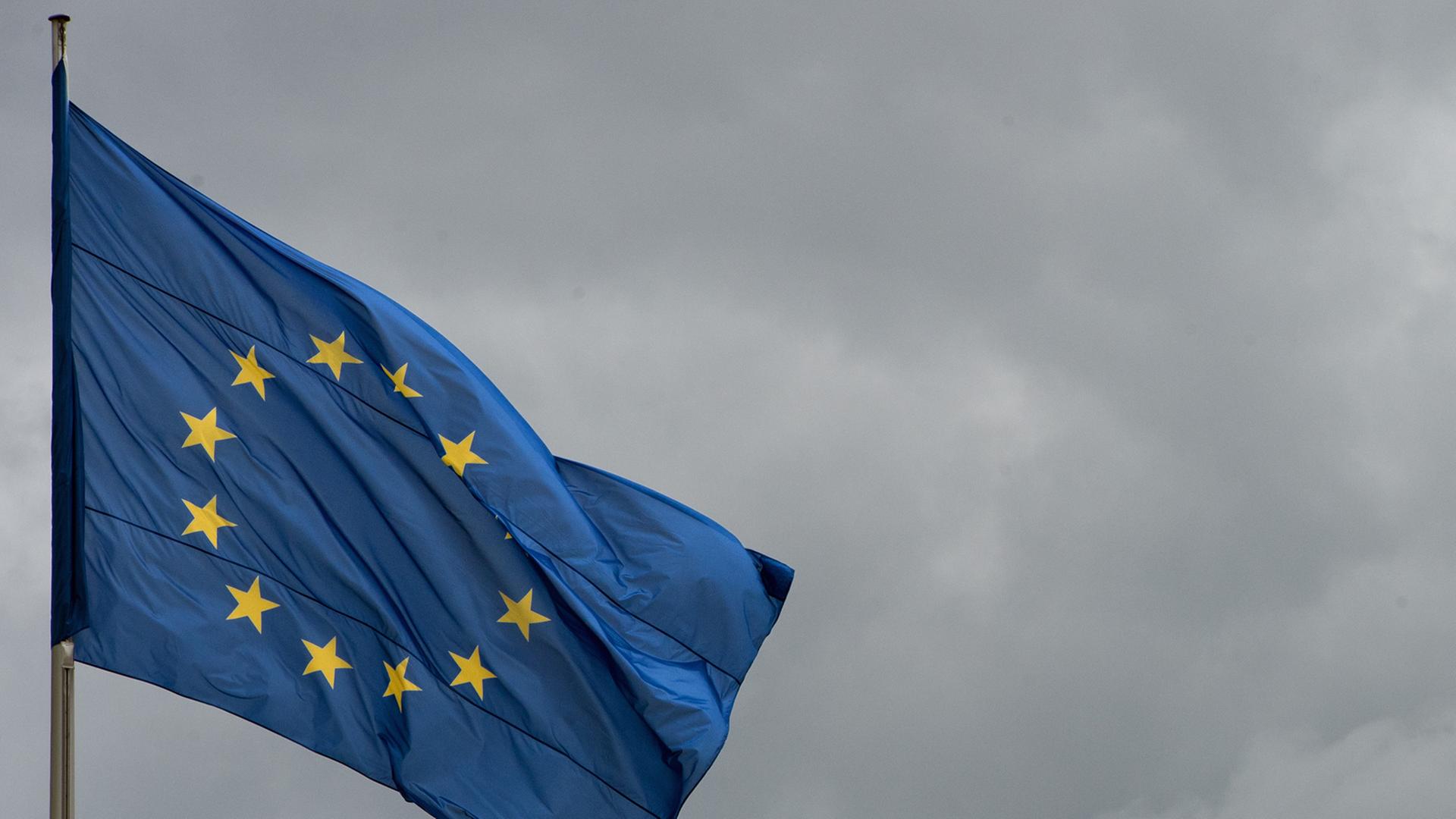 Die Flagge der Europäischen Union weht vor wolkenverhangenem Himmel.