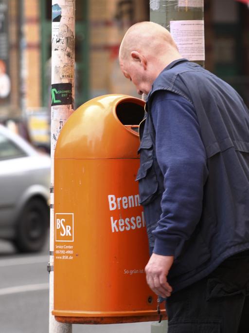 Ein Mann sucht in Berlin in einem Papierkorb nach Pfandflaschen oder Pfanddosen.