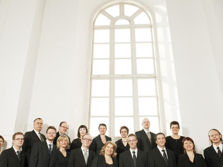 Der Chor steht in einem hellen Raum vor einem hohen Kirchenfenster.