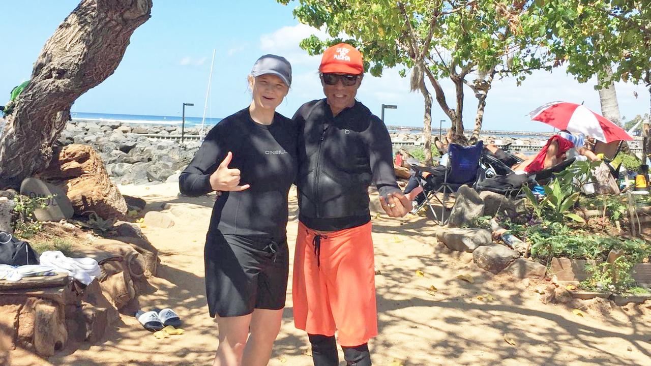 Nicole Markwald und Surflehrer Komi stehen am Strand und machen eine fröhliche Geste in Richtung Kamera.