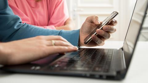 Ein Mann und eine Frau nutzen einen Laptop und ein Smartphone.
