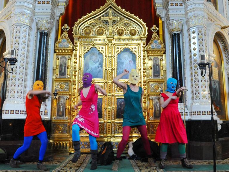 Das Bild zeigt die Musikerinnen von Pussy Riot bei ihrem inzwischen legendären Auftritt in einer Kirche in Moskau mit bunten Sturmhauben.