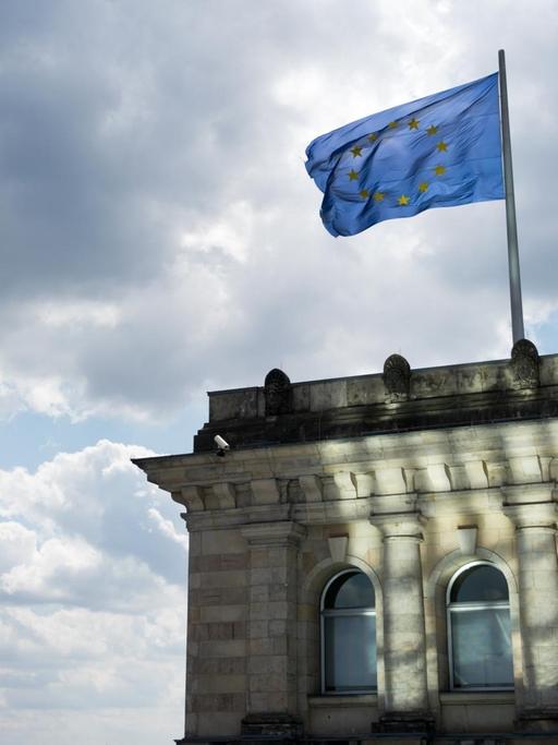 Eine Europaflagge weht am 06.07.2015 auf dem Dach des Deutschen Bundestages, dem Reichstagsgebäude, in Berlin vor dunklen Wolken.