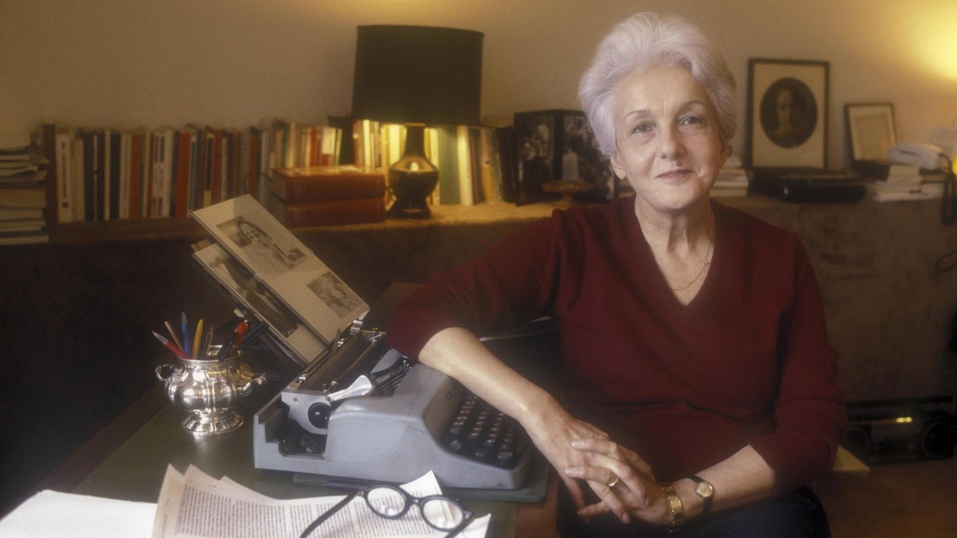 Eine ältere Frau sitzt an ihrem Schreibtisch, auf dem eine Schreibmaschine steht.