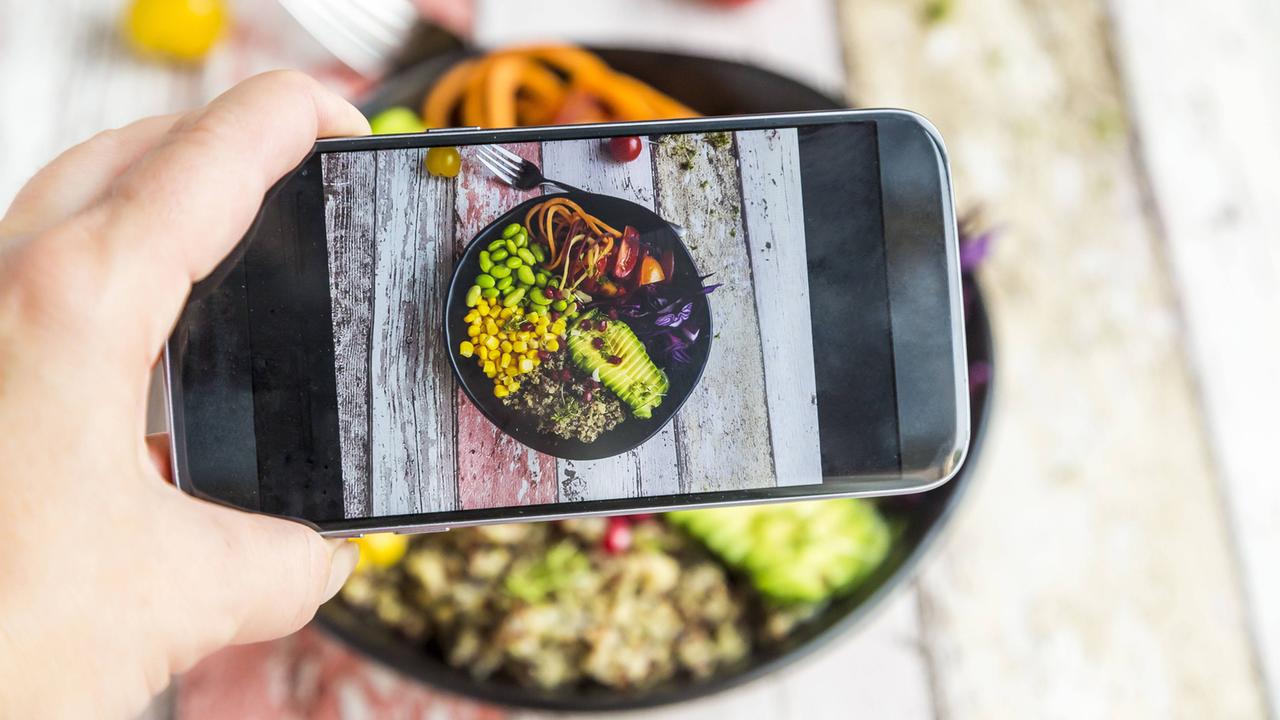 Eine Frau fotografiert ihre vegane Lunch bowl mit ihrem Smartphone.