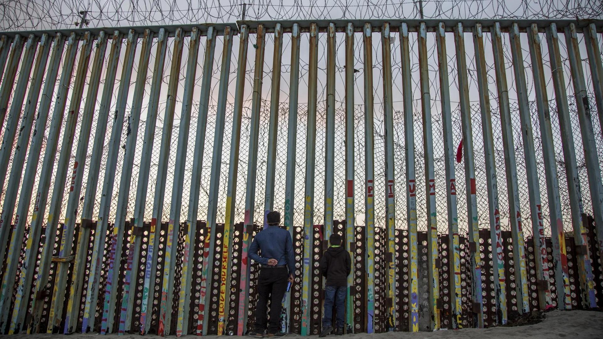 Ein Mann und sein Kind schauen durch die Grenzmauer in der mexikanischen Stadt Tijuana in Richtung US-Stadt San Diego.