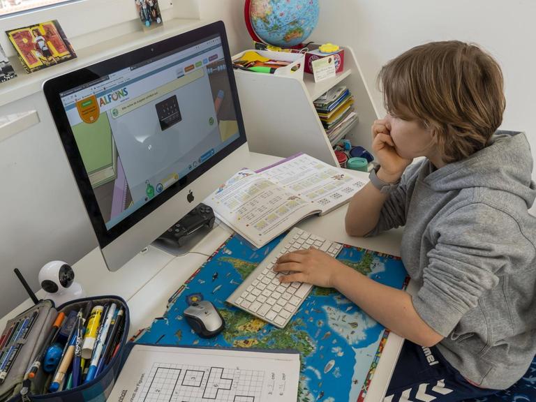 Ein Junge sitzt zu Hause an seinem Schreibtisch vor dem Computer und lernt