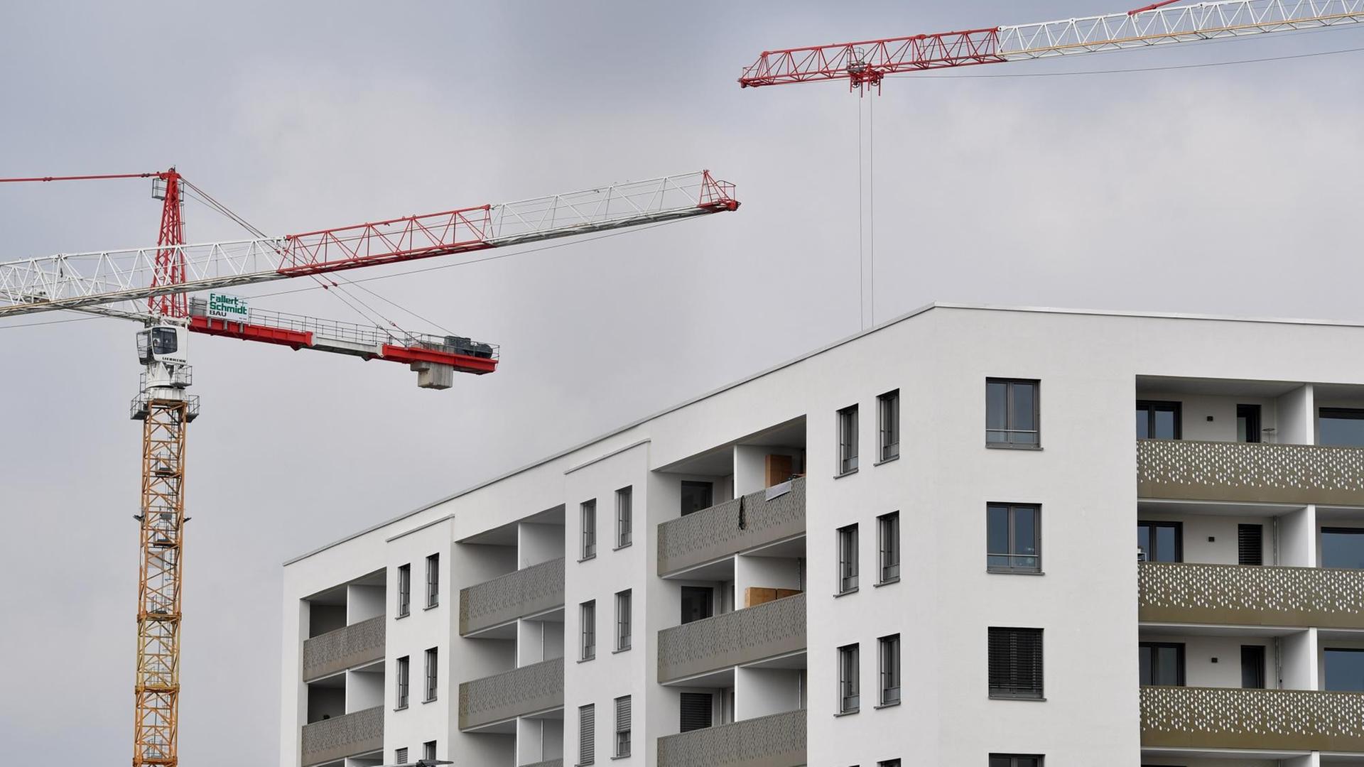 Baukräne vor einem weitgehend fertigestellten weißen Wohnbloick unter grauem Himmel. Baukräne vor einem weitgehend fertigestellten weißen Wohnbloick unter grauem Himmel.