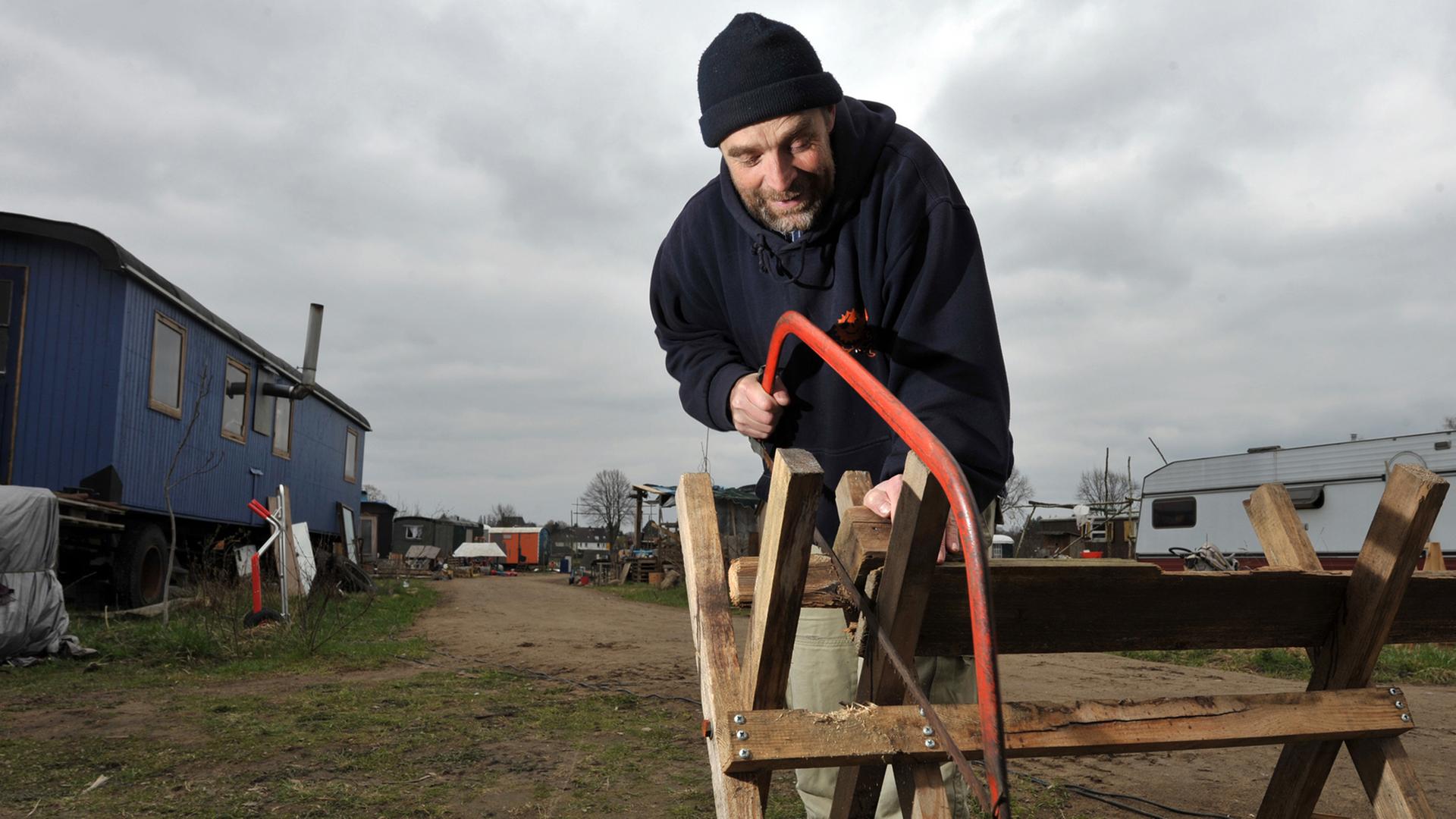 Ein Bewohner einer Wagenburg in Lüneburg sägt Brennholz.