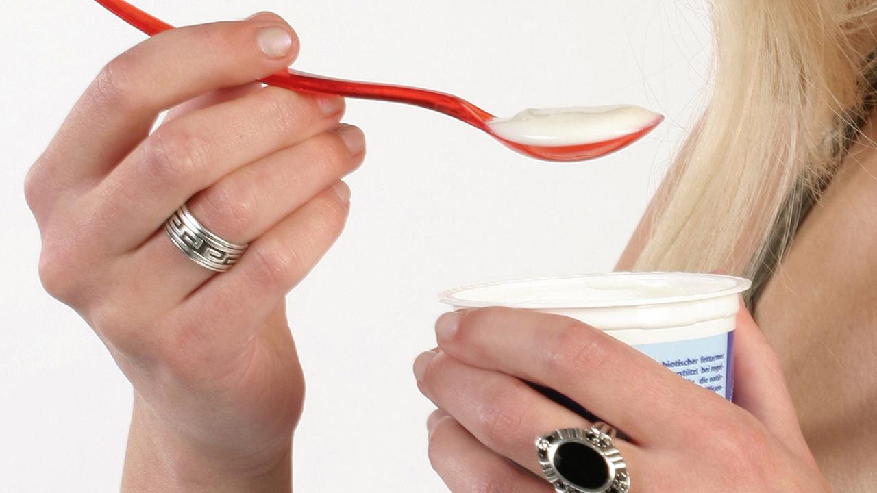Eine Hand hält einen roten Löffel mit Joghurt.
