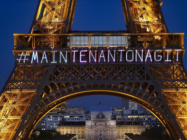 Der Eiffelturm wird mit dem Schriftzug "Maintenant on agit" angeleuchtet.