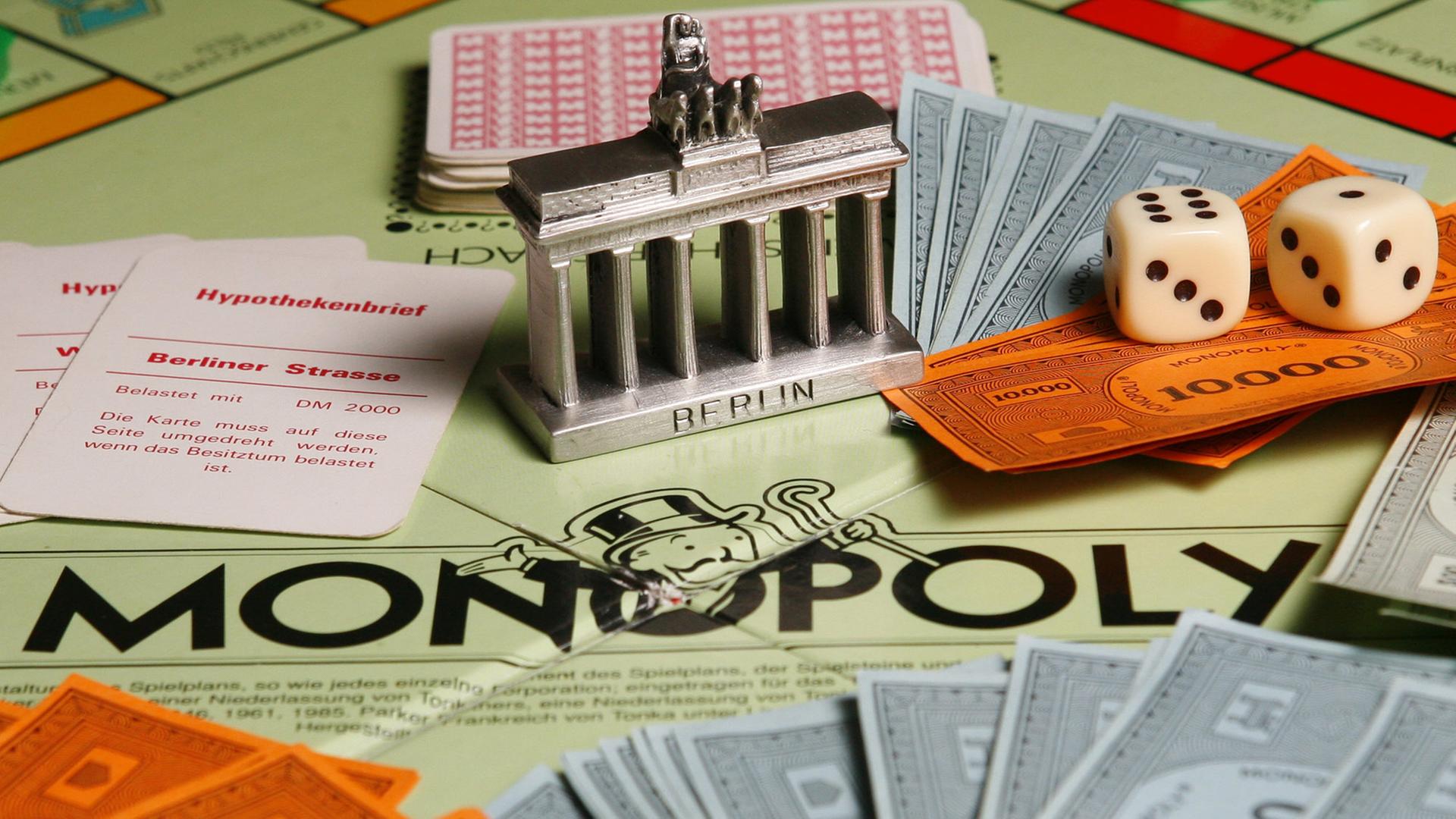 Ein Modell des Brandenburger Tores steht auf einem Monopoly-Brettspiel inmitten von Karten, Würfeln und Spielgeld-Scheinen.