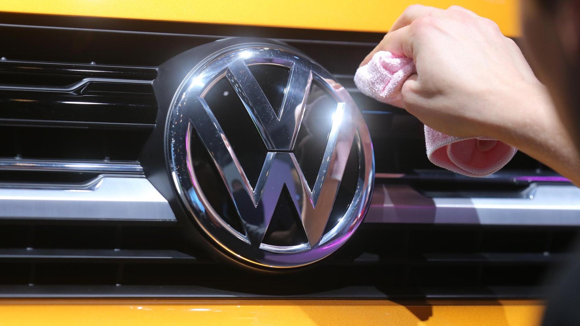 Ein Mitarbeiter von Volkswagen poliert am 12.03.2015 in Berlin vor Beginn der Jahres-Pressekonferenz das Logo an einem VW Sport Coupe.