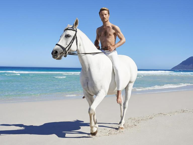 Andy Kassier auf einem weißen Pferd am Strand.