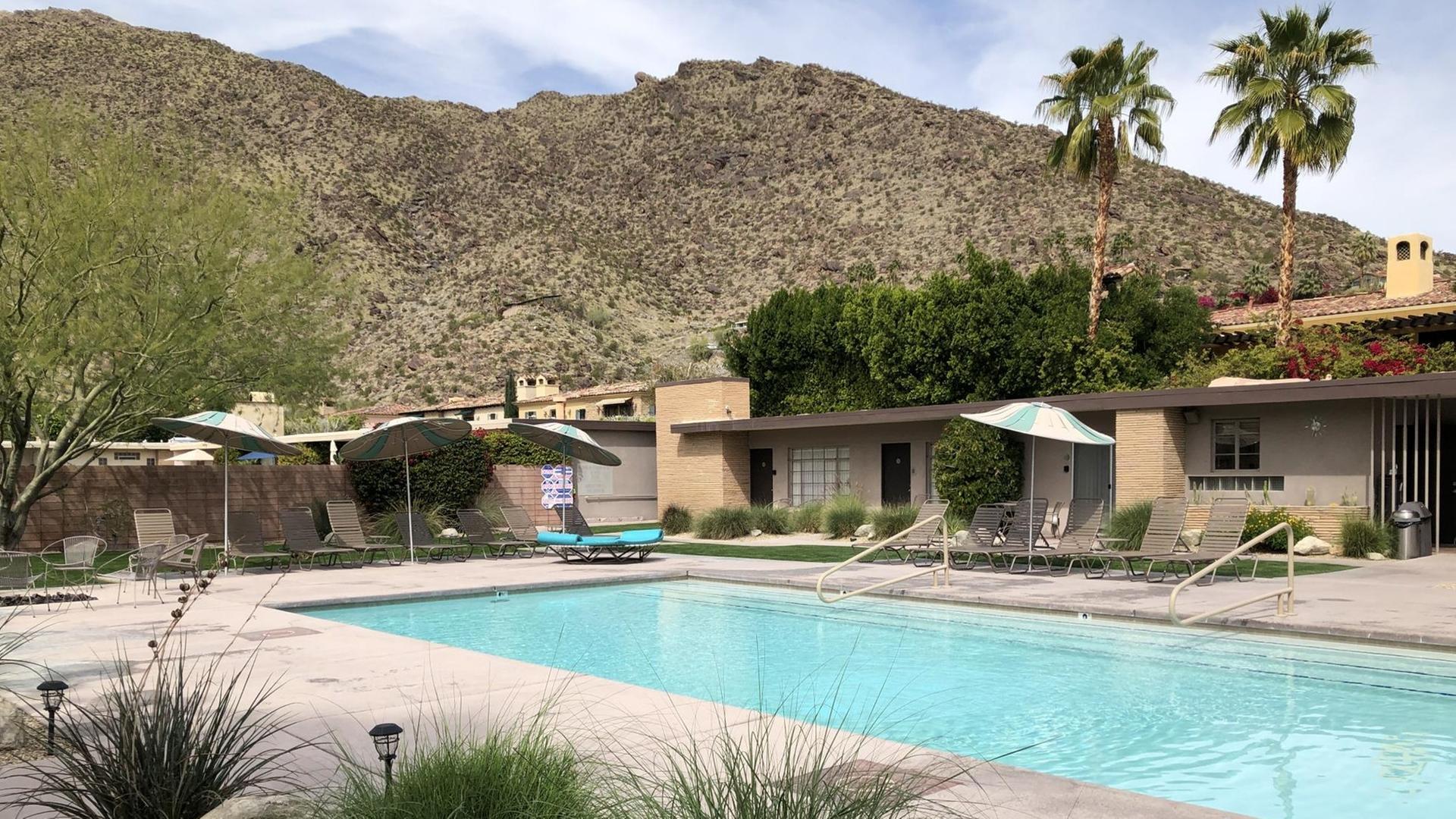 Ein Swimming Pool, umgeben von Architektur im internationalen Stil, vor der imposanten Kulisse eines Wüstengebirges.