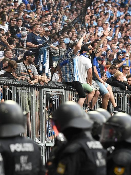Polizisten bewachen den Bereich vor Fans des TSV 1860 München, die auf dem Gitter sitzen.