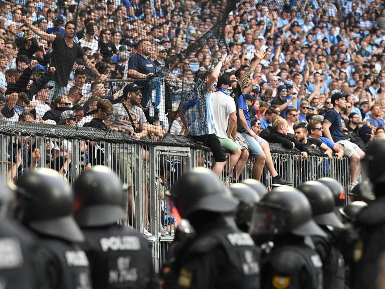 Polizisten bewachen den Bereich vor Fans des TSV 1860 München, die auf dem Gitter sitzen.