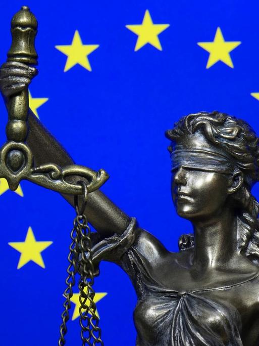 Eine Figur der Justitia vor der Fahne der Europäischen Union.