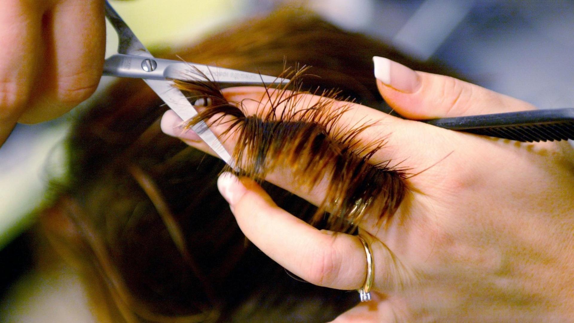 Einer jungen Frau werden in einem Friseursalon mit einer Schere die Haare geschnitten