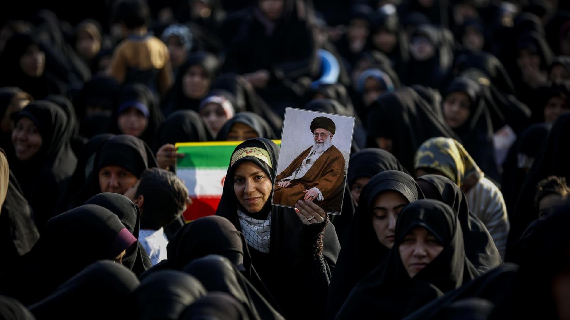 Frauen und Mädchen stehen am 31. Januar 2019 zusammen. Eine hält eine iranische Flagge hoch, eine andere das Bild von Revolutionsführer Ayatollah Khomeini