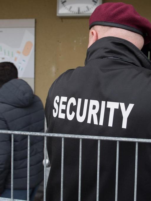 Zwei Sicherheitskräfte des Sicherheitsdienstleisters Siba Security GmbH, stehen im Februar in der Landeserstaufnahmeeinrichtung (LEA) in der Reinhardt-Kaserne in Ellwangen (Baden-Württemberg) an der Pforte, in der Mitte geht ein Flüchtling vorbei.