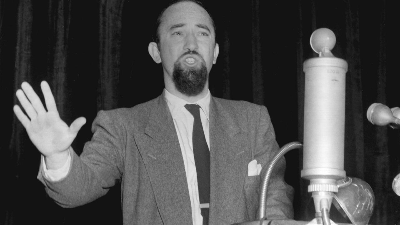 Ein Mann mit Kinnbart steht an einem Rednerpult, im Vordergrund ein Mikrofon.