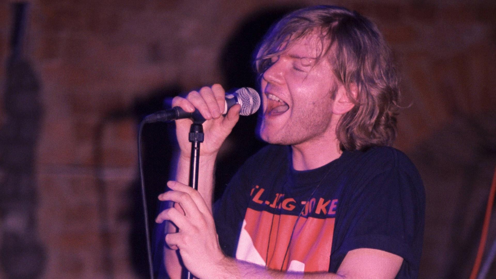 Der Sänger Rex Joswig hält singend ein Mikrofon in der Hand.