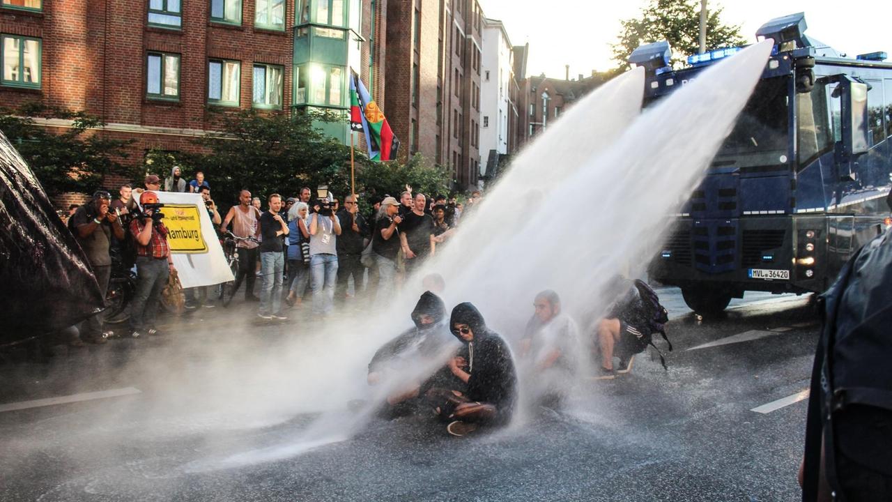 Wasserwerfer der Polizei sind auf Protestierende gerichtet, die die Straße mit einem Sitzstreik blockieren.